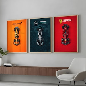 Könnte beinhalten: Drei gerahmte Poster von Formel-1-Autos. Das erste zeigt einen gelb-schwarzen McLaren-Wagen auf orangefarbenem Hintergrund. Das zweite zeigt einen silber-schwarzen Mercedes-Wagen auf türkisfarbenem Hintergrund. Das dritte zeigt einen roten Ferrari-Wagen auf rotem Hintergrund.