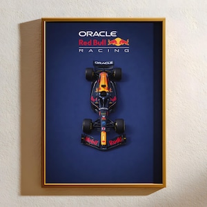 Peut inclure: Œuvre encadrée représentant une vue de dessus d'une voiture de Formule 1 Red Bull Racing. La voiture est principalement bleu marine, avec des détails rouges et jaunes. Le cadre est doré et le fond est bleu foncé. Les logos Oracle et Red Bull Racing sont visibles.