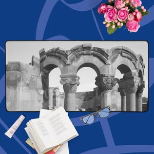 Puede incluir: Imagen en blanco y negro de una antigua estructura de piedra con aberturas arqueadas y columnas ornamentadas. Un ramo de rosas rosas, gafas de sol con tinte azul, un libro abierto y un tubo de crema también están presentes.