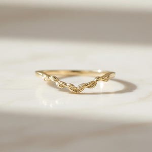 May include: A gold-colored ring with a curved, leaf-like design. The ring's band is thin, and the leaves are intricately detailed. The ring is set against a light-colored background, highlighting its delicate features.