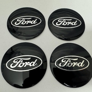 Può includere: Quattro coprimozzi Ford neri con logo Ford argentato. I coprimozzi sono rotondi e lucidi, con il logo Ford in un ovale bianco. I coprimozzi sono disposti in una formazione quadrata.