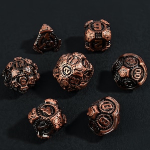 Könnte beinhalten: Ein Satz von sieben kupferfarbenen Würfeln mit Steampunk-Design. Jeder Würfel weist komplizierte Zahnrad- und Zahnraddetails auf, wobei die Zahlen deutlich sichtbar sind. Die Würfel sind auf einer dunklen Oberfläche angeordnet, was ihre metallische Oberfläche zeigt.
