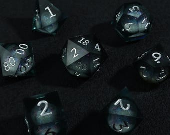 Könnte beinhalten: Ein Satz von sieben polyedrischen Würfeln mit einem galaxieartigen Design. Die Würfel sind dunkelgrün mit silbernen Zahlen und einem wirbelnden, kosmischen Inneren. Das Set enthält einen D4, D6, D8, D10, D12, D20 und einen Prozentwürfel.