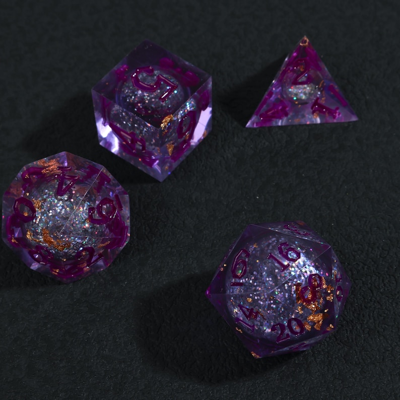 May include: Four polyhedral dice sets in a purple and silver glitter design. The dice are transparent with purple numbers and gold flakes. The dice are for tabletop games.