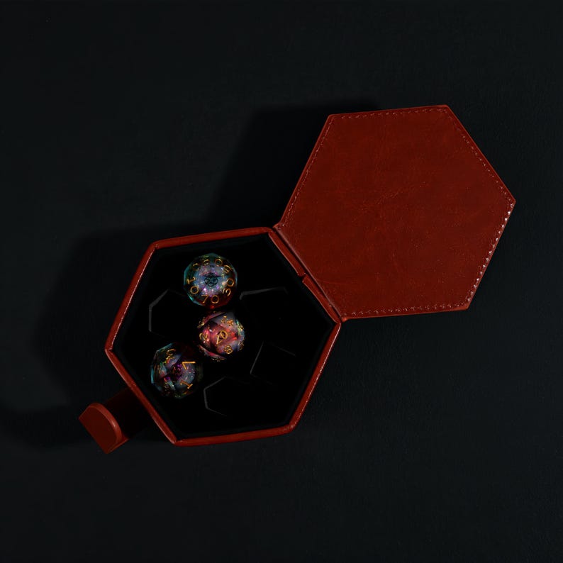 May include: A red leather hexagonal dice case, open to reveal three multi-colored, spherical dice. The dice have gold-colored numbers and intricate designs. The case is on a black background.