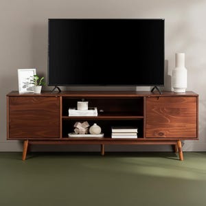 Könnte beinhalten: Ein TV-Schrank im Mid-Century-Modern-Stil in dunkler Braun-Ausführung. Der Schrank verfügt über zwei Schränke, offene Regale und konische Beine. Ein großer schwarzer Fernseher steht oben, mit dekorativen Gegenständen.