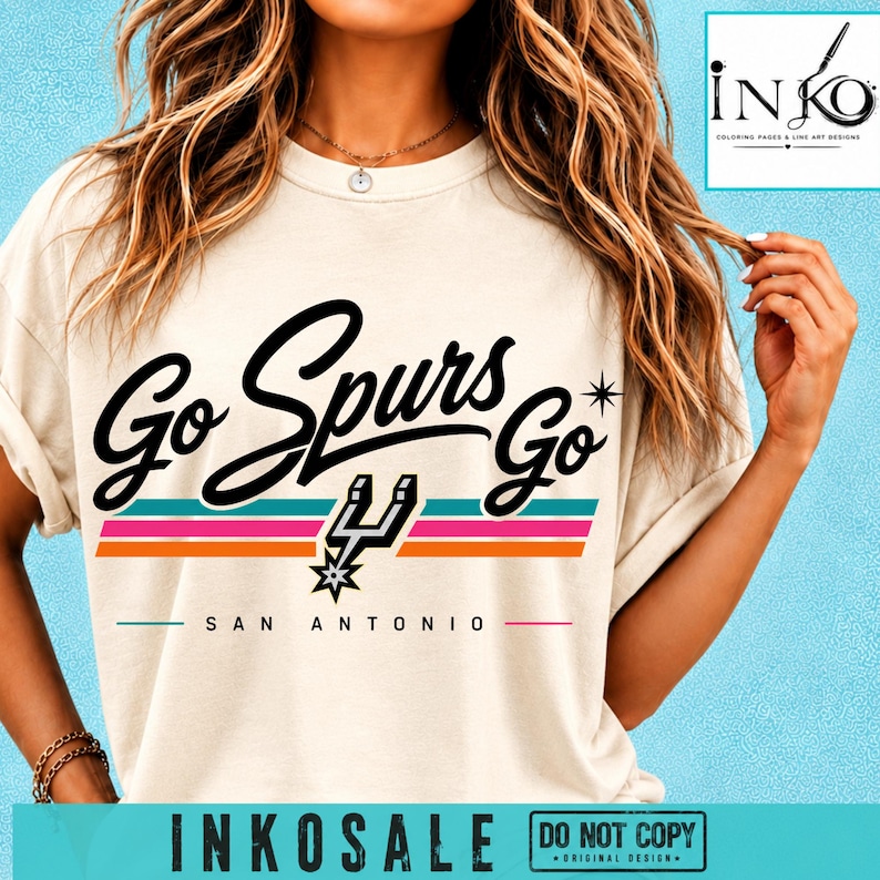 May include: A cream-colored t-shirt featuring the black text Go Spurs Go with a star icon, a San Antonio team logo, and horizontal stripes in teal, pink, and orange. The text San Antonio is printed below the graphic in a simple black font.