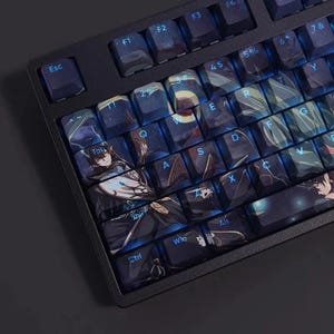 Op de afbeelding: Een zwart mechanisch toetsenbord met aangepaste keycaps met anime-kunstwerk. De keycaps hebben een donkerblauw en zwart kleurenschema met verlichte letters. Het toetsenbord heeft een standaardindeling met functietoetsen.