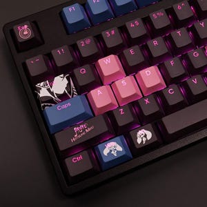 Puede incluir: Teclado mecánico negro con teclas rosas y azules. Las teclas "WASD" son rosas. Algunas teclas tienen gráficos y texto de estilo anime, incluyendo "Caps" y "Hatsune Miku". El teclado tiene un marco negro y retroiluminación púrpura.