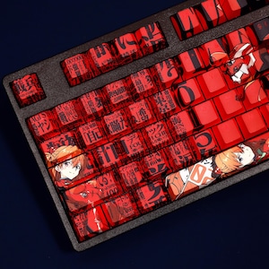 May include: A black mechanical keyboard with red keycaps. The keycaps feature Japanese text and anime character illustrations. The keyboard has a standard layout with a variety of keycap designs and colours.