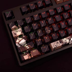 Puede incluir: Teclado mecánico negro con teclas personalizadas con arte de personajes de estilo anime. Las teclas tienen un fondo oscuro con ilustraciones coloridas. El teclado tiene un marco negro e iluminación roja.