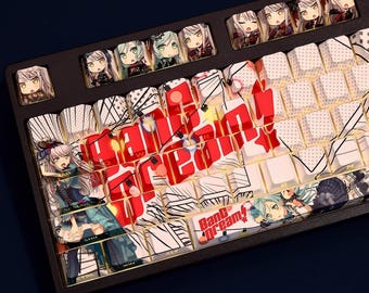 Op de afbeelding: Zwart mechanisch toetsenbord met aangepaste keycaps met anime-stijl illustraties. De keycaps tonen karakters en de tekst "BanG Dream!" in rood en wit. Sommige toetsen hebben een zwart-wit patroon.