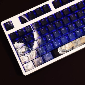 May include: A white mechanical keyboard with custom keycaps. The keycaps feature anime-style artwork and a space-themed design with blue backlighting. The keyboard has a standard layout with function keys and a number pad.