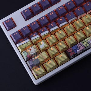 May include: A white mechanical keyboard with purple and yellow keycaps. The keycaps have a striped pattern and anime character designs. The keyboard has orange backlighting, and the text "KESSER&BAN" is visible.