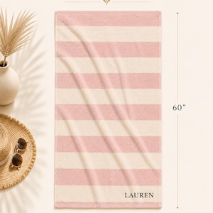 Op de afbeelding: Gepersonaliseerde strandlaken met horizontale strepen in lichtroze en cr&egrave;me. De handdoek is 152 cm lang en 76 cm breed, met de naam "LAUREN" rechtsonder.