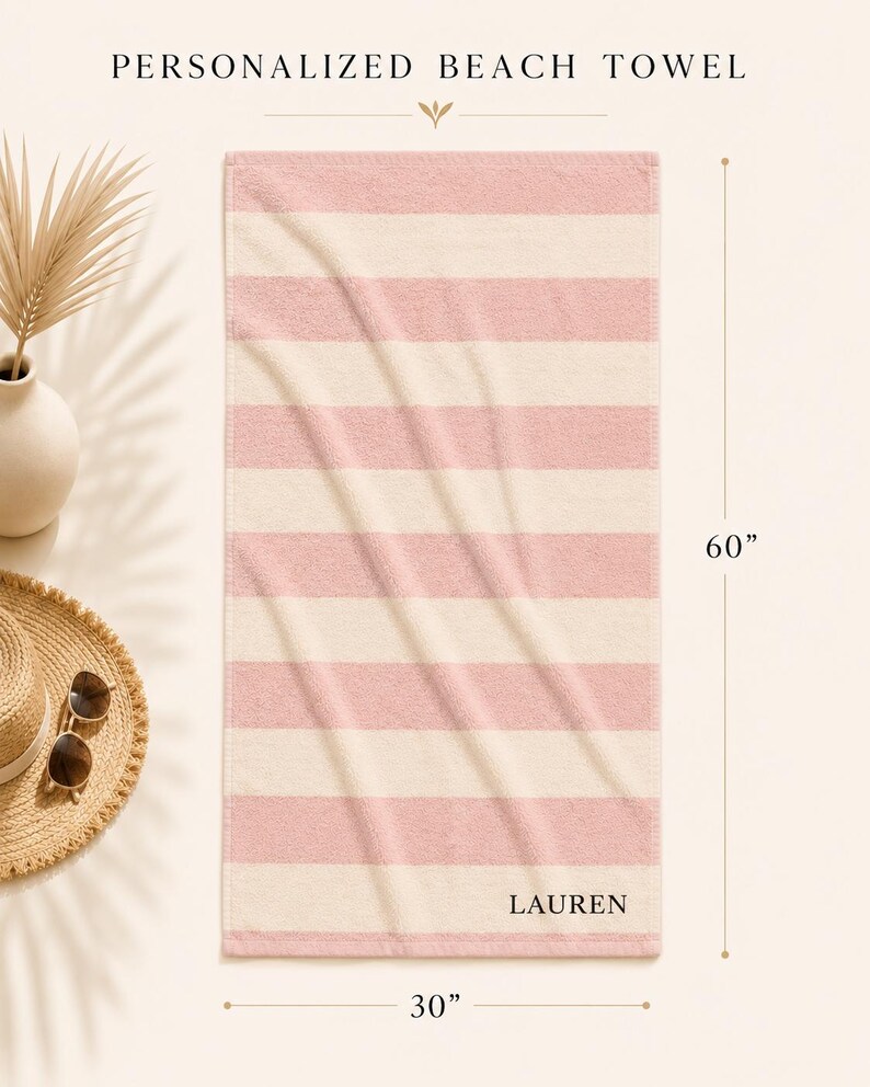 Op de afbeelding: Gepersonaliseerde strandlaken met horizontale strepen in lichtroze en cr&egrave;me. De handdoek is 152 cm lang en 76 cm breed, met de naam "LAUREN" rechtsonder.