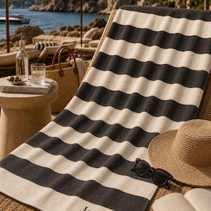 May include: A rectangular beach towel featuring horizontal black and cream stripes. The towel is personalized with the name Jessica embroidered in black thread near the bottom edge. The fabric has a soft, plush texture throughout the entire surface.