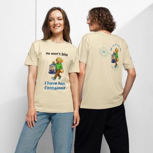 May include: Beige t-shirts with a cartoon dog carrying a cage with a person inside. The front of the shirt says "He won't bite, I have him contained." The back of the shirt has a similar design and text.
