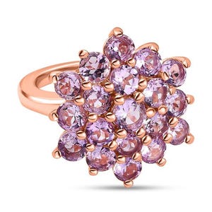 May include: A rose gold ring featuring a cluster of round, light purple gemstones. The gemstones are arranged in a floral pattern, creating a sparkling and eye-catching design. The ring's band is a smooth, polished rose gold.