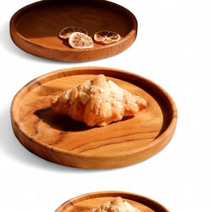 Puede incluir: Bandejas de madera para servir con vetas naturales. Una bandeja contiene un cruasán cubierto con almendras laminadas. Otra bandeja contiene rodajas de cítricos secos. Las bandejas son redondas con borde elevado.