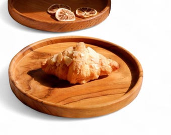 May include: Wooden serving trays with a natural wood grain. One tray holds a croissant topped with sliced almonds. Another tray holds dried citrus slices. The trays are round with a raised edge.