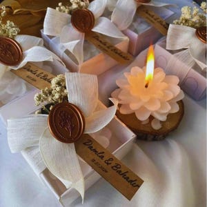 Può includere: Scatole regalo quadrate bianche decorate con nastri in tessuto bianco, fiori secchi di gipsofila e sigilli in ceralacca color rame con un motivo floreale. Ogni scatola include un'etichetta in carta marrone con il testo Damla & Bahadir 13.07.2024.