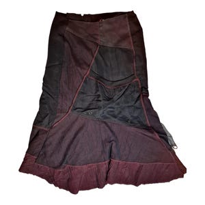 Pode incluir: Saia patchwork em tons de bordô e preto. A saia apresenta um design único com painéis contrastantes e costuras vermelhas. O tecido parece ser uma combinação de ganga e outros materiais, criando um visual texturizado. A saia tem uma bainha rodada.