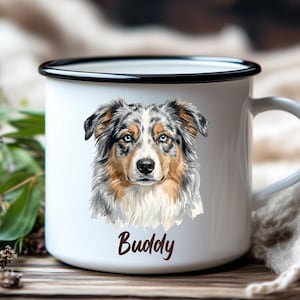 Könnte beinhalten: Ein weißer Emaillebecher mit schwarzem Rand, der eine detaillierte Illustration eines Australian Shepherd mit blauen Augen und braunem, grauem und weißem Fell zeigt. Unter dem Hund ist der Name Buddy in einer dunkelbraunen Schreibschrift gedruckt.