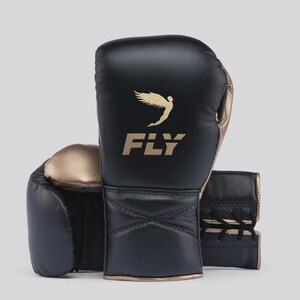 Può includere: Guantoni da boxe neri con dettagli dorati. I guantoni presentano la scritta "FLY" in lettere dorate, accompagnata da un logo di uccello dorato. Realizzati in pelle, hanno una chiusura con lacci.