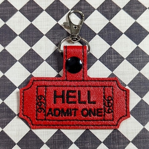May include: Red leather keychain with a black stitched ticket design that says "HELL ADMIT ONE".