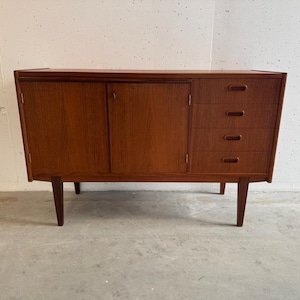 Op de afbeelding: Een houten kast in mid-century modern stijl met een warme bruine afwerking. De kast heeft een deur aan de linkerkant en drie lades aan de rechterkant. Hij staat op vier schuine poten, wat bijdraagt aan de retro-esthetiek. De kast is ongeveer 102 cm breed.