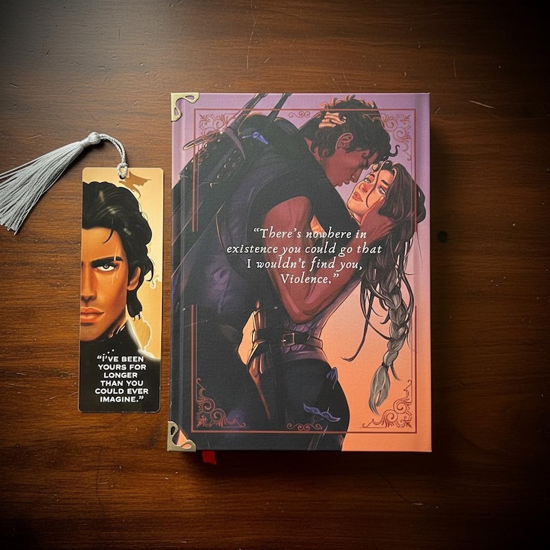 May include: A hardcover book and a bookmark with a tassel. The book cover features a romantic illustration of a couple embracing, with the quote "There's nowhere in existence you could go that I wouldn't find you, Violence." The bookmark has a portrait and a quote.