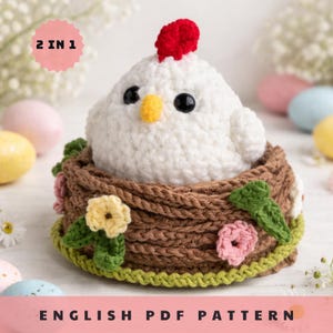 May include: A crocheted white chicken with a red comb and yellow beak sits in a brown nest adorned with green leaves and pink and yellow flowers. The text "2 IN 1" is in a pink circle. The text "ENGLISH PDF PATTERN" is at the bottom.