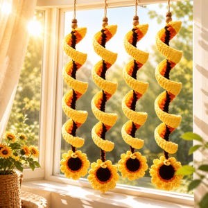 May include: Crocheted sunflower spiral hanging decorations. Each spiral is yellow, orange, and black, with a wooden bead at the top and a sunflower at the bottom. The decorations hang in front of a window with sunlight.