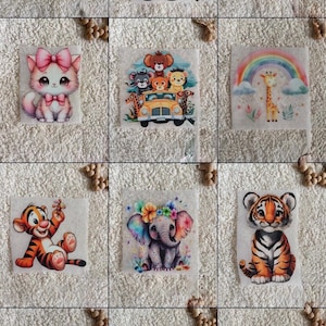 May include: A collection of colorful, whimsical iron-on patches featuring various animal characters. Designs include a teddy bear with aviator goggles, a cat with a pink bow, and a tiger cub. The patches are on a white background.