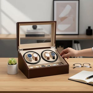 May include: A brown watch winder with a glass top, showcasing four automatic watches on black rotating holders. The interior features a beige lining and a lower compartment for additional watches. A small succulent plant sits to the left.