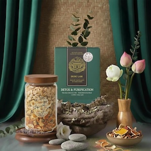 Può includere: Un barattolo di vetro con coperchio in legno pieno di erbe e fiori secchi. Una scatola verde con la scritta "Detox & Purification" è dietro il barattolo. Un piccolo vaso di legno contiene fiori di loto.