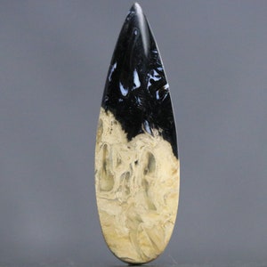 May include: A polished, teardrop-shaped gemstone with a striking contrast. The top half is a glossy black, transitioning to a creamy beige with intricate patterns. The stone's elongated form is ideal for jewelry or display.