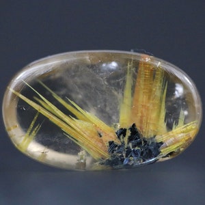 May include: A clear, oval-shaped gemstone with internal inclusions of yellow, orange, and black minerals. The gemstone has a polished surface and a translucent appearance, showcasing the intricate patterns within.