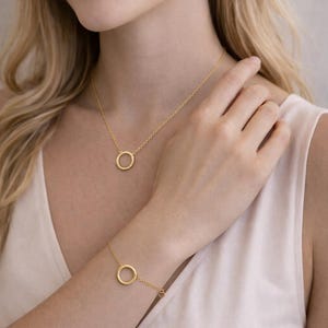 Könnte beinhalten: Goldfarbenes Schmuckset mit Halskette, Armband und Ohrringen. Jedes Schmuckstück hat ein kreisförmiges Design mit einem strukturierten, seilartigen Muster. Die Halskette liegt um den Hals, das Armband am Handgelenk und die Ohrringe sind kleine Creolen.
