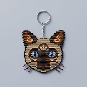 May include: A Siamese cat head keychain crafted from small square beads. The design features a cream-colored face with dark brown ears, a dark brown nose and muzzle area, and bright light blue eyes. A silver metal ring is attached to the top.