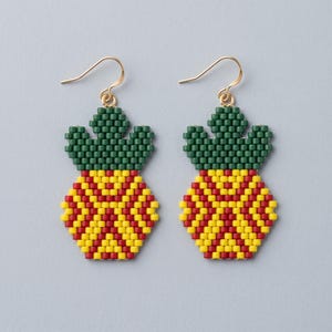 May include: A pair of drop earrings crafted from small beads in the shape of a pineapple. The top section is dark green, while the bottom section features a geometric pattern of yellow and red beads. Each earring hangs from a gold-tone hook.