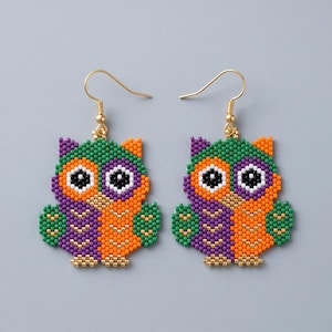 Può includere: Un paio di orecchini pendenti a forma di gufo realizzati con piccole perline multicolori. I gufi presentano sezioni verdi, viola e arancioni con grandi occhi bianchi e neri, sospesi a ganci in metallo dorato per orecchie forate.