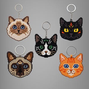 Puede incluir: Cinco llaveros con forma de gato hechos de pequeñas cuentas. La colección incluye un gato crema y marrón con ojos azules, un gato negro con ojos amarillos, un gato blanco y negro con ojos verdes, un gato tipo siamés y un gato atigrado naranja.