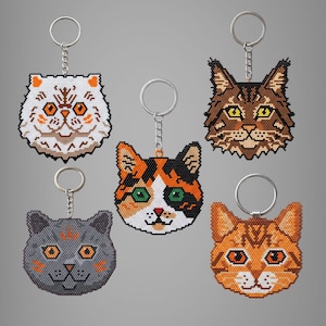 May include: Five cat-shaped keyrings crafted from small beads. The collection includes a white cat with orange eyes, a brown tabby, a grey cat with orange eyes, a calico cat with green eyes, and an orange tabby cat with orange eyes.