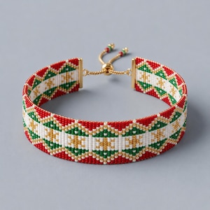 May include: A woven bead bracelet featuring a geometric pattern in red, white, green, and gold. The bracelet has a gold-toned metal sliding clasp mechanism with small beads at the ends of the adjustable pull cords for a secure fit on the wrist.