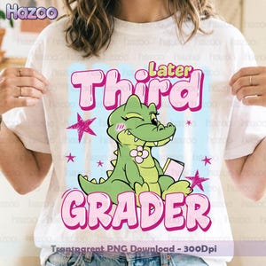 Könnte beinhalten: Weißes T-Shirt mit einem Cartoon-Alligator, der ein Buch hält, zwinkert und eine Blume trägt. Das Shirt hat die Worte "Later Third Grader" in rosa Blasenbuchstaben mit Sternen.