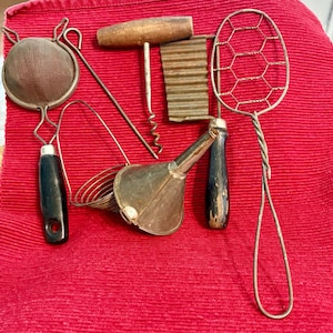 May include: A collection of vintage kitchen tools including a mesh strainer with a black handle, a wooden-handled corkscrew, a metal grater, a metal funnel, and a wire skimmer with a long twisted handle, all featuring aged metal surfaces.