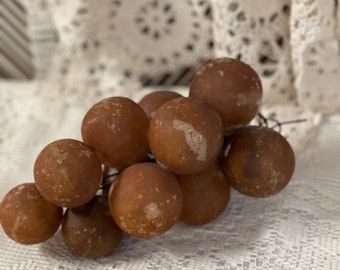May include: A cluster of brown, round, ceramic grapes on a white crocheted surface.