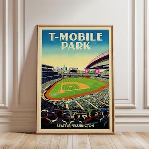 May include: A framed art print featuring a stylised illustration of T-Mobile Park in Seattle, Washington. The image shows a baseball stadium with a green field, blue sky, and spectators in the foreground. The text reads T-MOBILE PARK.